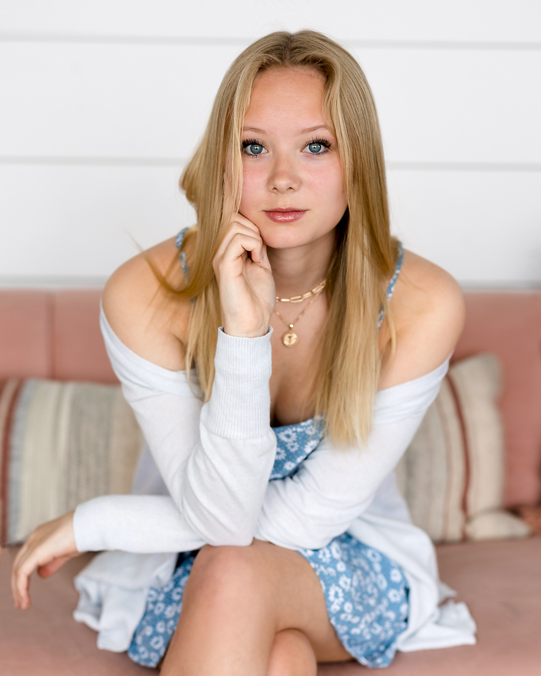 studio image of a teen with gorgeous blue eyes sitting on a pink couch